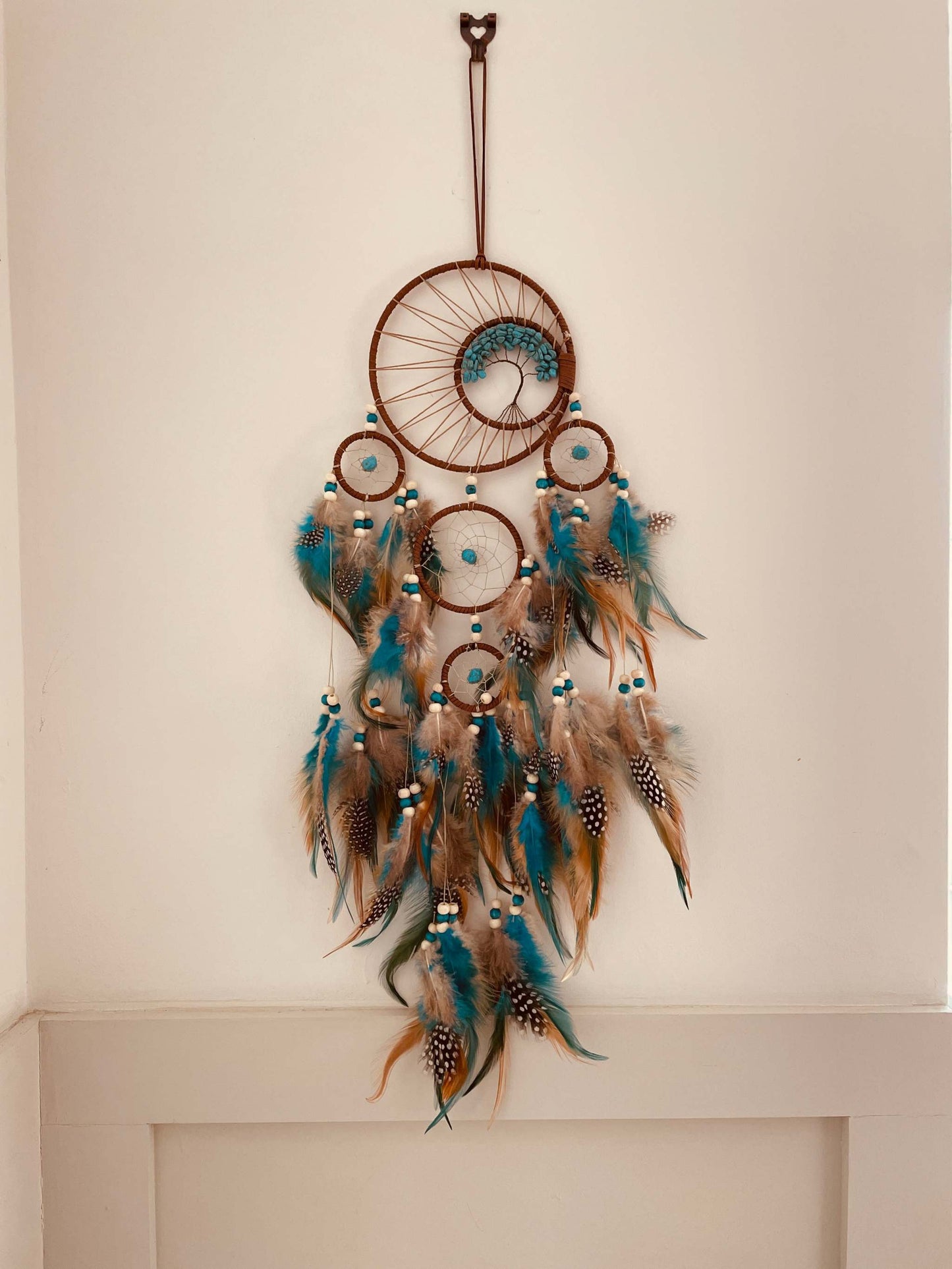 Tree of Life Dream Catcher with blue and brown feathers hanging on wall.