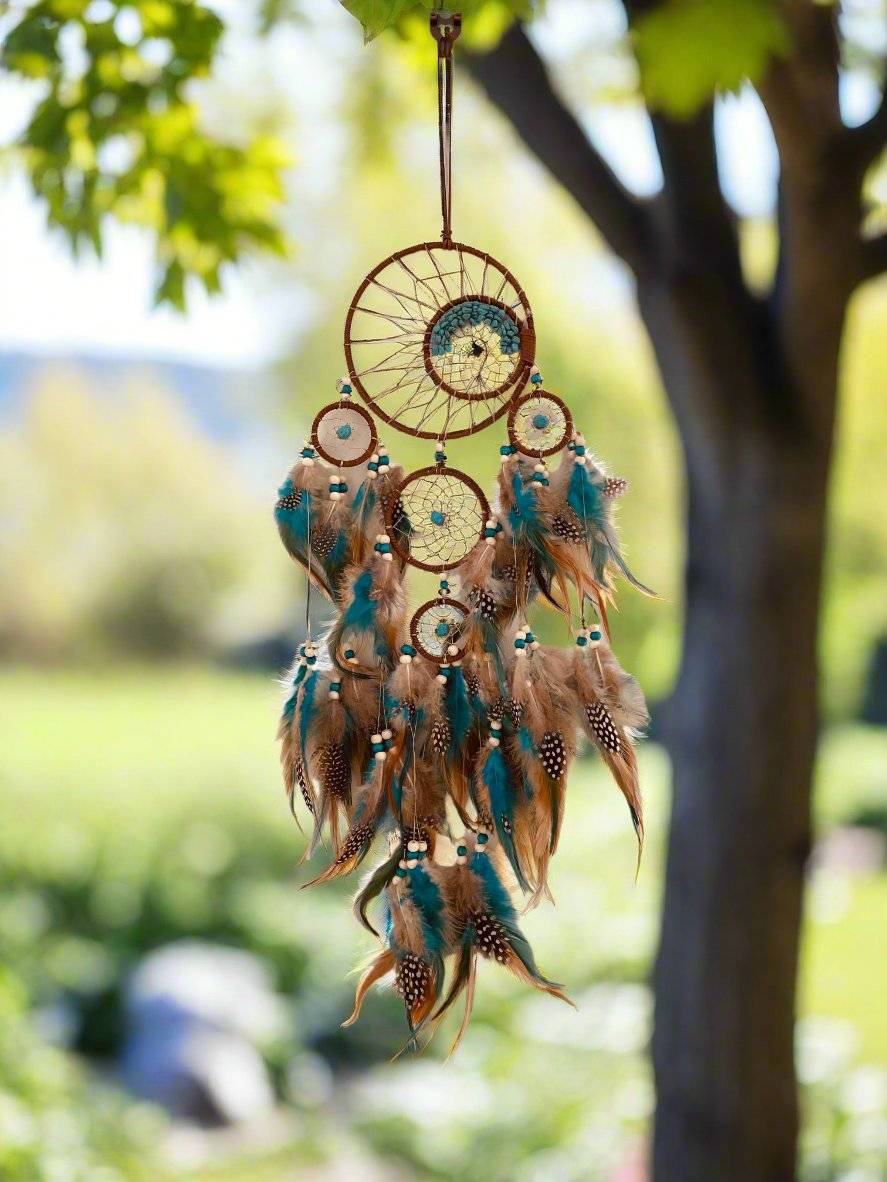 Tree of Life Dream Catcher with blue and brown feathers hanging outdoors.