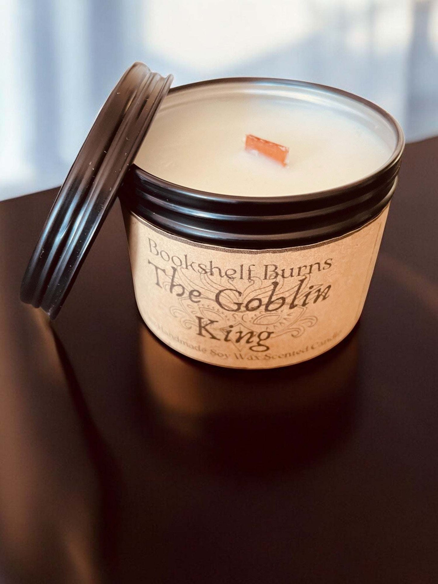 Hand-poured scented candle in a tin labeled "The Goblin King," inspired by classic stories, with a wooden wick.