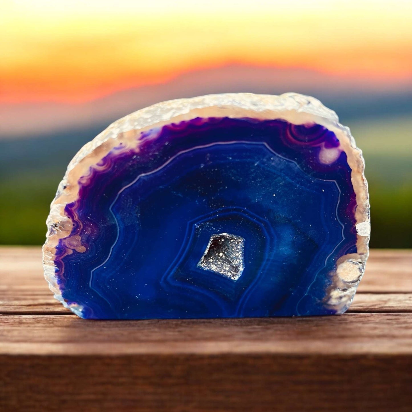 Brazilian Cut Agate displaying vibrant colors and crystal formations against a scenic background.
