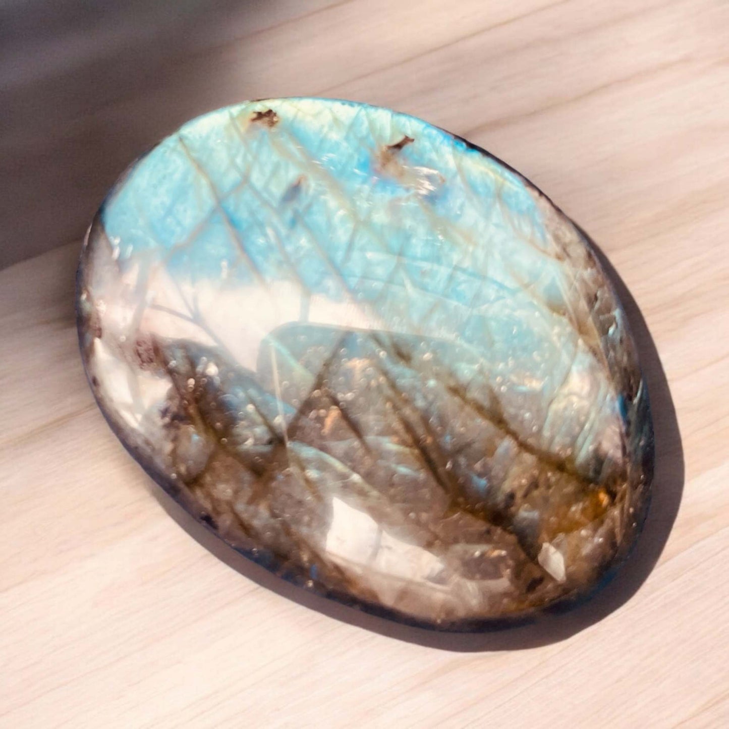 Labradorite palm stone with iridescent flashes of blue and gold on a wooden surface.