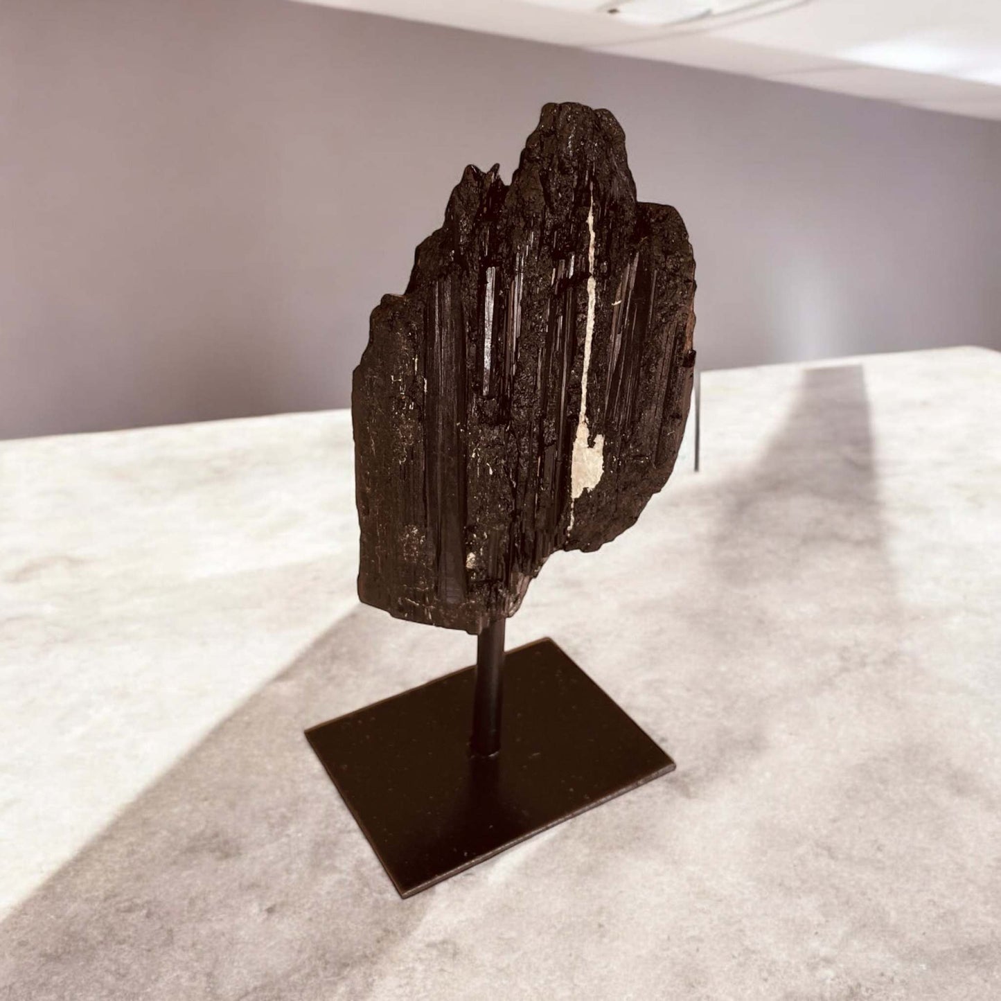 Black Tourmaline on a stand, known for its shielding properties and energetic barrier against negativity.