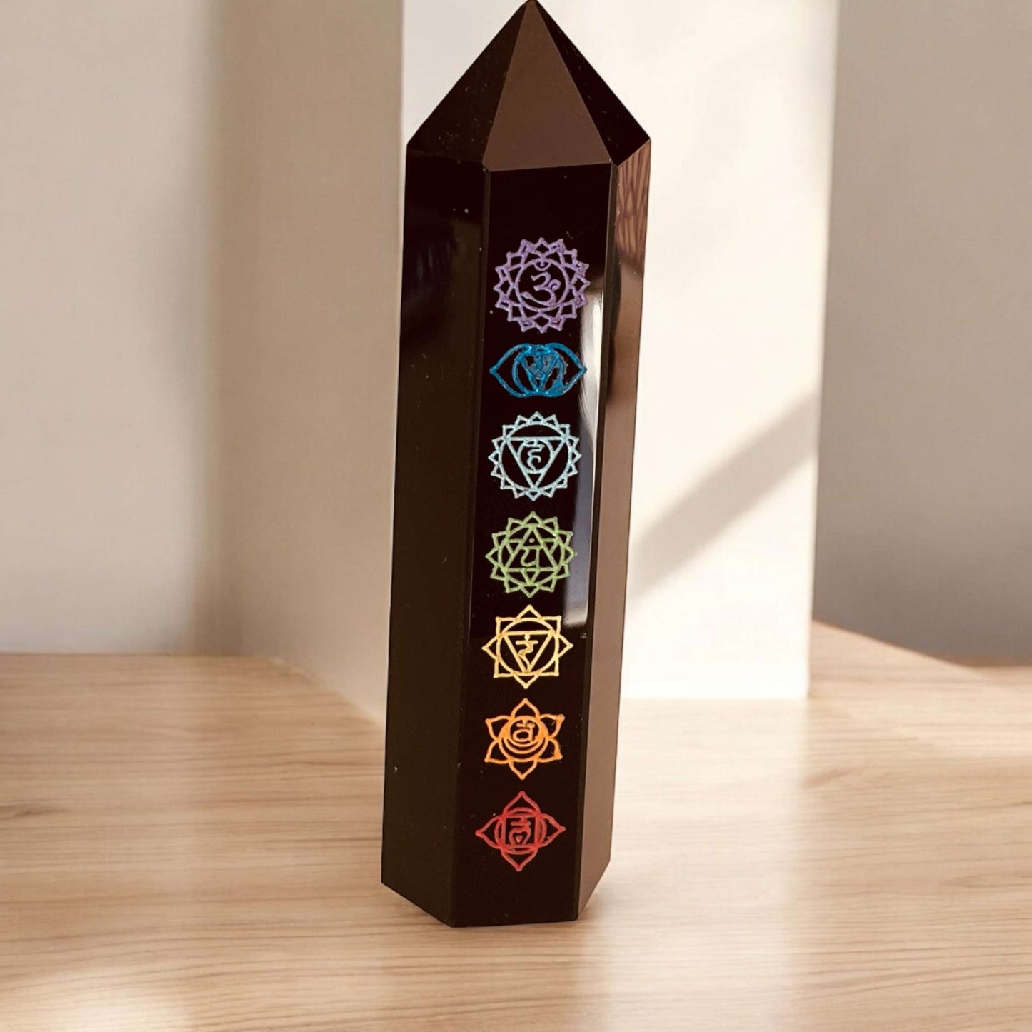 Chakra Obsidian Point crystal with chakra symbols on wooden surface.